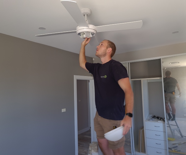 Electrician installing a ceiling fan in a residential room