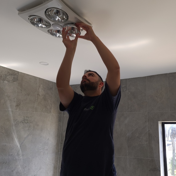 Electrician installing a ceiling heat lamp and light fixture in a bathroom.